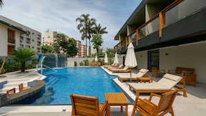 A rooftop pool area with lounge chairs and umbrellas, surrounded by buildings and palm trees. - Marmeu Tropical Ltda (Guarujá)