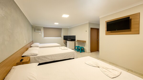 A hotel room with two beds, a small kitchenette, a TV mounted on the wall, and a bathroom door.