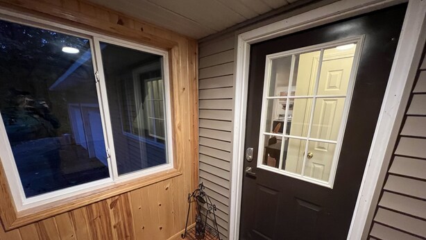 Una puerta principal con un panel de vidrio, un pequeño porche con un banco, y una ventana que da a una vista exterior.