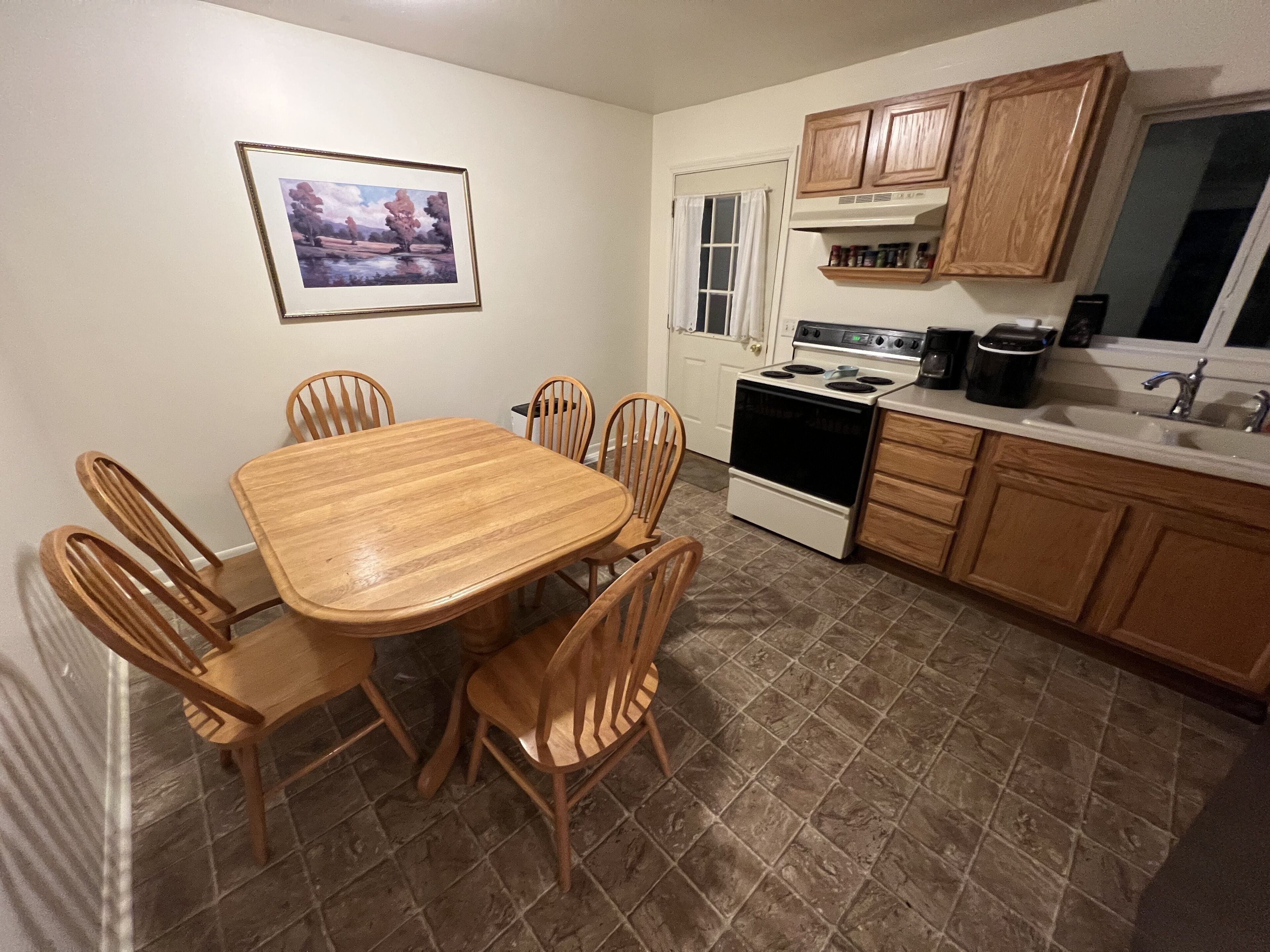 A kitchen with a wooden table and chairs, a stove, cabinets, and a window with curtains.