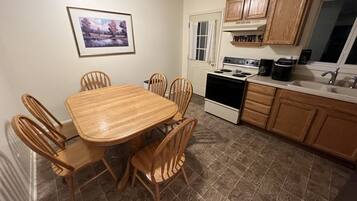 A kitchen with a wooden table and chairs, a stove, cabinets, and a window with curtains.