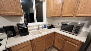 Una cocina con armarios de madera, microondas, cafetera y ventana.