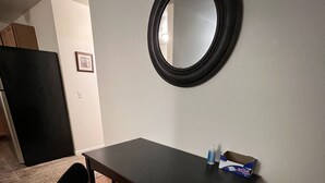 Un espacio de oficina pequeño con un escritorio, una silla de oficina negra, un espejo redondo en la pared y una caja de mascarillas sobre el escritorio.