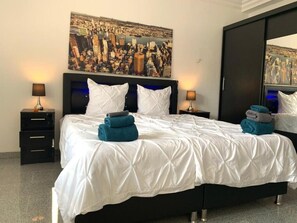 Habitación de hotel con una cama grande, dos mesitas de noche, un cuadro en la pared y un espejo.