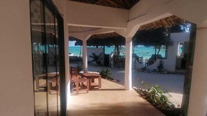 Uma área de estar coberta ao ar livre, com mesas e cadeiras, com vista para uma praia e oceano.
