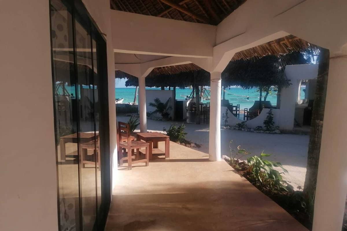 Un espace extérieur abrité, doté de tables et de chaises, offrant une vue dégagée sur la plage et l’océan.