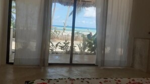 Quarto com cama coberta de pétalas de rosa, vista para a praia e estrutura de telhado de palha externa.