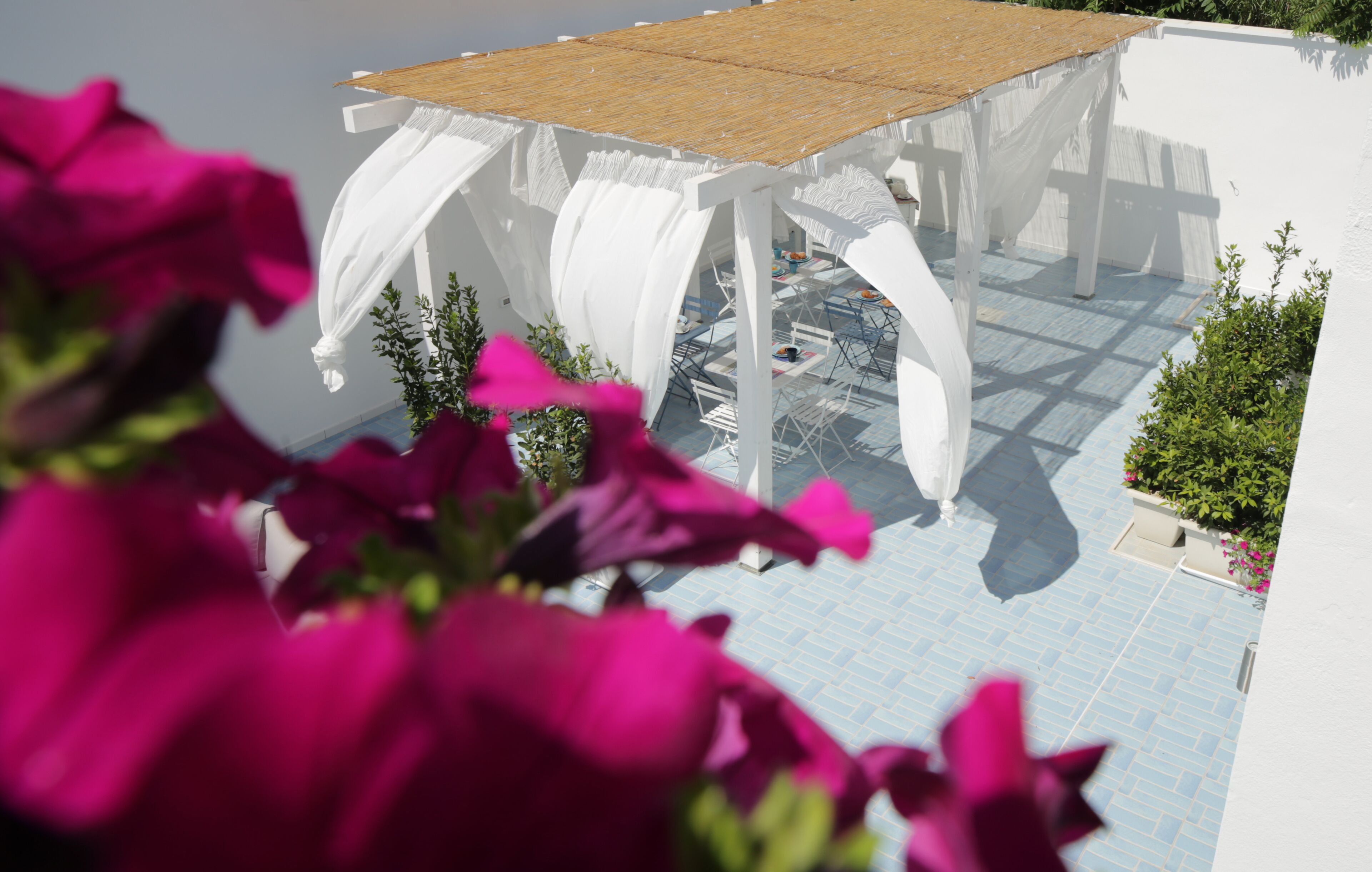 A white outdoor seating area with a wooden table, surrounded by white columns and blue tiles.