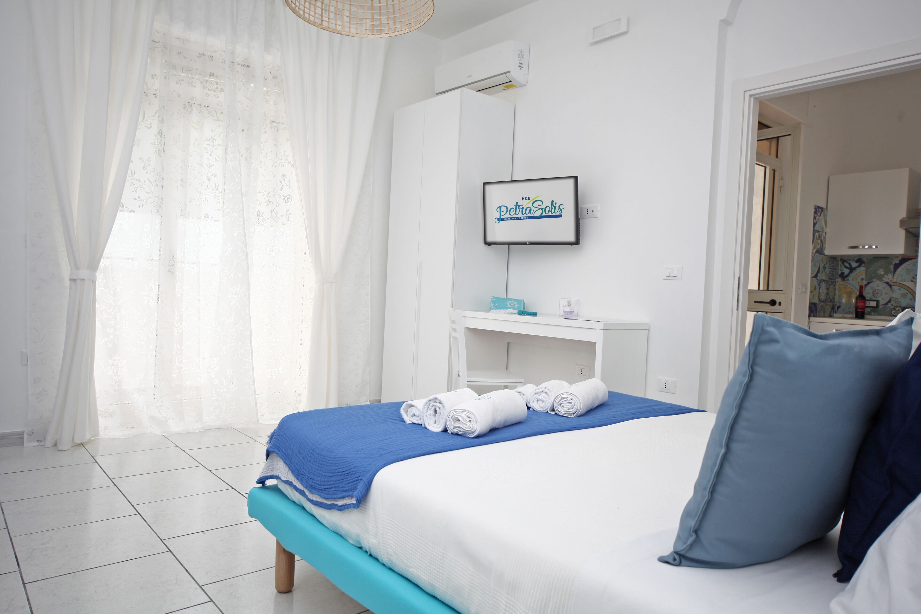 A neatly made bed with rolled towels, a blue accent pillow, and a framed sign on the wall.