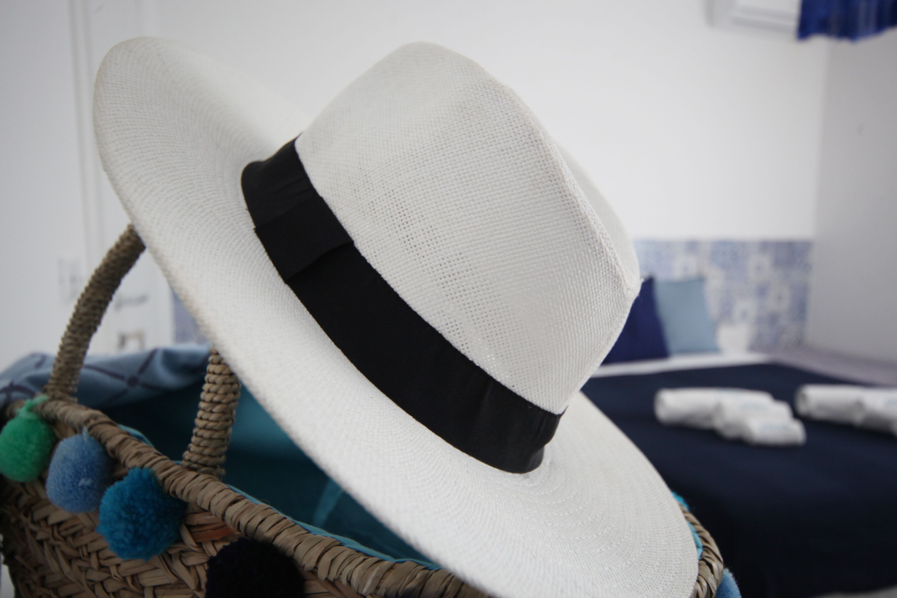Un sombrero blanco con cinta negra sobre una cesta trenzada.