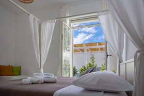 A bedroom with a bed, white curtains, and a view of greenery outside. - Petra Solis (Manduria)