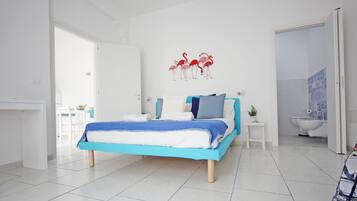 A modern bedroom with a bed, a white door, a bathroom with a toilet, and a wall with a flamingo decoration.