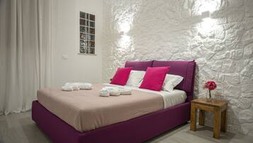A bedroom with a bed, pillows, a nightstand, a vase with a flower, and a window with a view of the outside.
