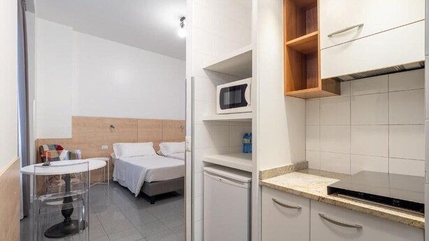 A compact hotel room with a bed, a small round table, a microwave, a dishwasher, and a kitchenette with a countertop and cabinets. - one-room apartment navigli accommodation (Milano)