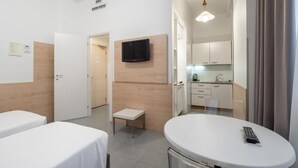 A hotel room with two single beds, a small table, a TV mounted on the wall, and a kitchenette in the background. - one-room apartment navigli accommodation (Milano)