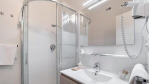 A modern bathroom with a glass shower enclosure, a white sink, and a mirror with a hairdryer. - one-room apartment navigli accommodation (Milano)