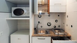 A compact kitchen with a microwave, sink, and built-in oven. There are shelves above the microwave and a dish rack above the sink. - one-room apartment navigli accommodation (Milano)