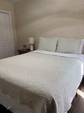 Una cama con colcha, una mesita de noche con lámpara y una puerta.