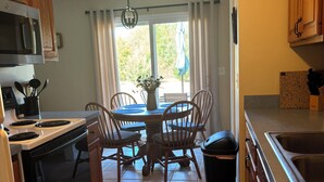 Une cuisine équipée d’une table à manger, de chaises, d’une poubelle, d’un four à micro-ondes et d’une cuisinière.