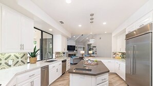 Una cocina moderna con armarios blancos, una isla central, electrodomésticos de acero inoxidable y un salpicadero con diseño.