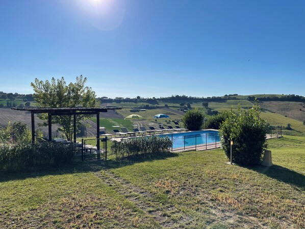 A pool area with a pergola, sun loungers, and a view of rolling hills.