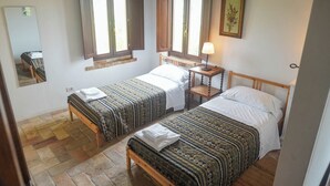 Ein Zimmer mit zwei Einzelbetten, einem Nachttisch mit Lampe, einem Spiegel und einem Fenster mit Fensterläden.