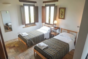 A room with two single beds, a bedside table with a lamp, a mirror, and a window with shutters.