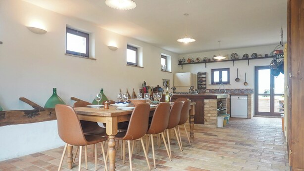 Ein Essbereich mit Holztisch und Stühlen, im Hintergrund eine Küche und ein Boden aus Ziegelsteinen.