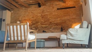 Ein gemütliches Zimmer mit freiliegenden Backsteinwänden, Holzbalkendecke und einer komfortablen Sitzecke mit Sessel und Sofa.