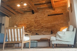 A cozy room with exposed brick walls, a wooden ceiling, and a comfortable seating area with a chair and sofa.