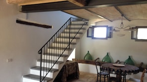 A staircase with a metal railing leading to a landing. There is a dining table with chairs and a patterned tablecloth. Green vases are on the table.