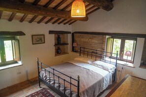 A bedroom with a bed, a window, a shelf with a vase, and a hanging light fixture.