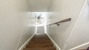Una escalera de madera con barandilla, que lleva a una habitación donde se ve una bicicleta al fondo.