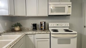 Una cocina con gabinetes blancos, una estufa blanca, un microondas, una cafetera y una planta en la encimera.