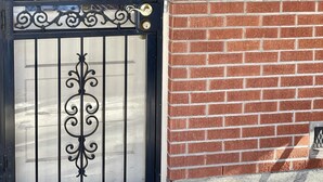Una reja de metal negro con detalles de hierro forjado, un muro de ladrillo y una lámpara fijada a la pared.
