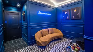 A room with a blue wall, a neon sign, a sofa, and a patterned floor. - Palazzetto Trevi (Rome)