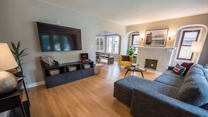 A modern living room with a grey sofa, wooden flooring, a flat-screen TV, a black entertainment unit, and a yellow armchair.