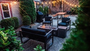 An outdoor patio with a fire pit, seating, and string lights.