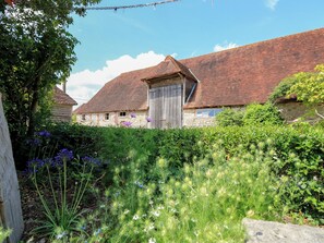 A rustic building with a red-tiled roof, surrounded by lush greenery and flowering plants. - Byre Cottage 3 (Pulborough)