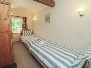 A bedroom with a single bed, a wooden wardrobe, a window with curtains, a wall-mounted light, and a framed picture. - Byre Cottage 3 (Pulborough)