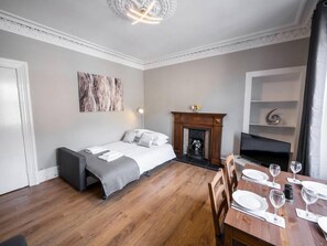 A modern bedroom with a bed, a fireplace, a dining table set for two, and a TV mounted on the wall.