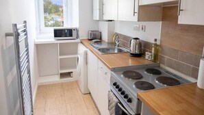 Pieni, käytännöllinen keittiö, jossa on valkoiset kaapit, mikroaaltouuni, leivänpaahdin, vedenkeitin ja liesi.