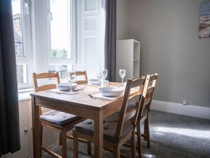A dining table set for four with wooden chairs, a white cabinet in the background, and a view of the outside through a window.
