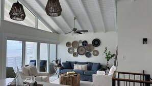 Un salón amplio con techo alto, ventilador de techo y gran ventana con vista al océano.