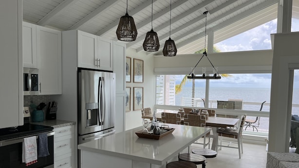 Una cocina moderna con una isla grande, armarios blancos y vista al océano.