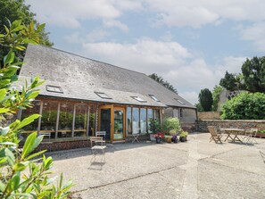 A building with a sloped roof, large windows, and a gravel patio with outdoor seating. - Byre Cottage 4 (Pulborough)