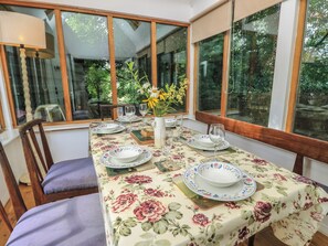 Una mesa de comedor dispuesta con platos, vasos y un florero, con vistas al verdor exterior.