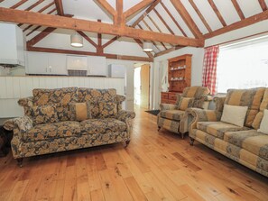 Uma sala ampla com piso de madeira, um sofá estampado com flores, uma poltrona listrada e um armário de madeira com xícaras de chá.