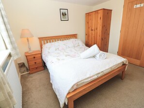 A bedroom with a wooden bed, a nightstand, a lamp, a wardrobe, and a framed picture on the wall.