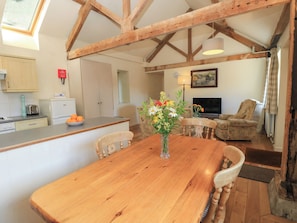 A wooden dining table with chairs, a kitchen area with a toaster, and a living room with a television. - Byre Cottage 2 (Pulborough)